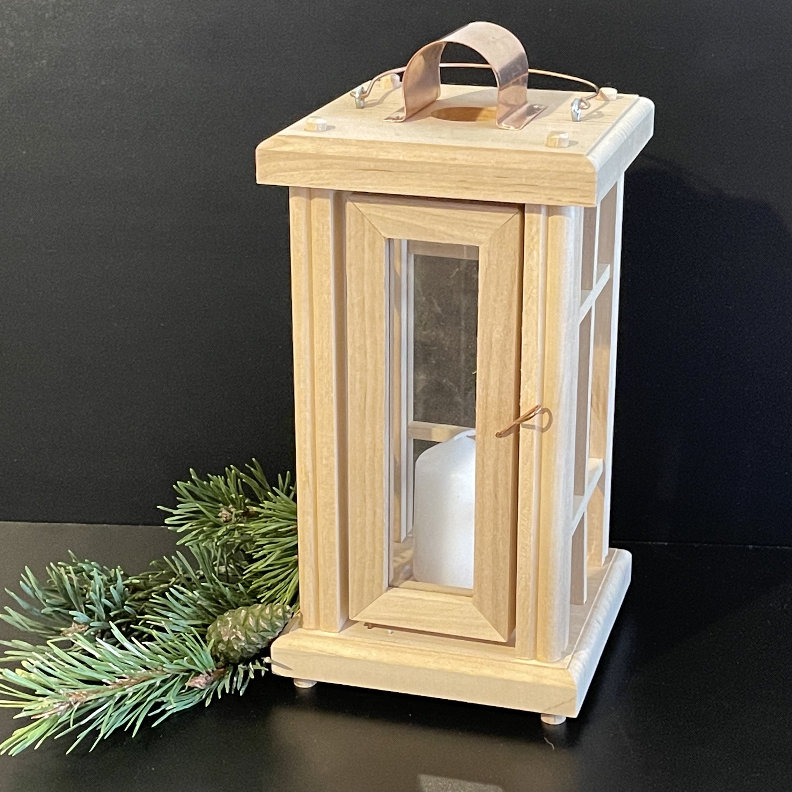 kleine Laterne aus Holz naturbelassen mit Glaseinsätzen und Fenstergitter. Kleine Drehtür. Aufhängung, Kerzenteller und Schließe aus Kupfer.